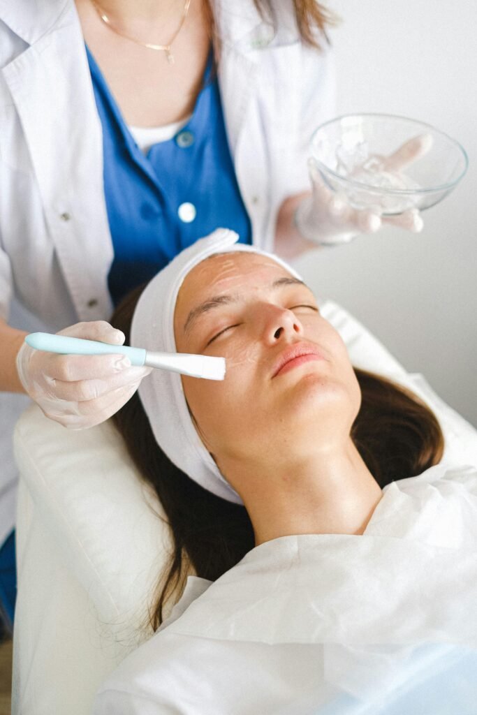 From above of crop cosmetician putting moisturizing lotion on face during beauty procedure in salon