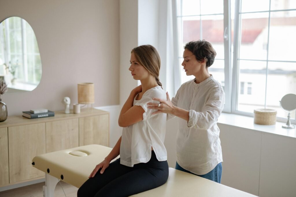 A massage therapist providing shoulder treatment to a woman in a well-lit studio.